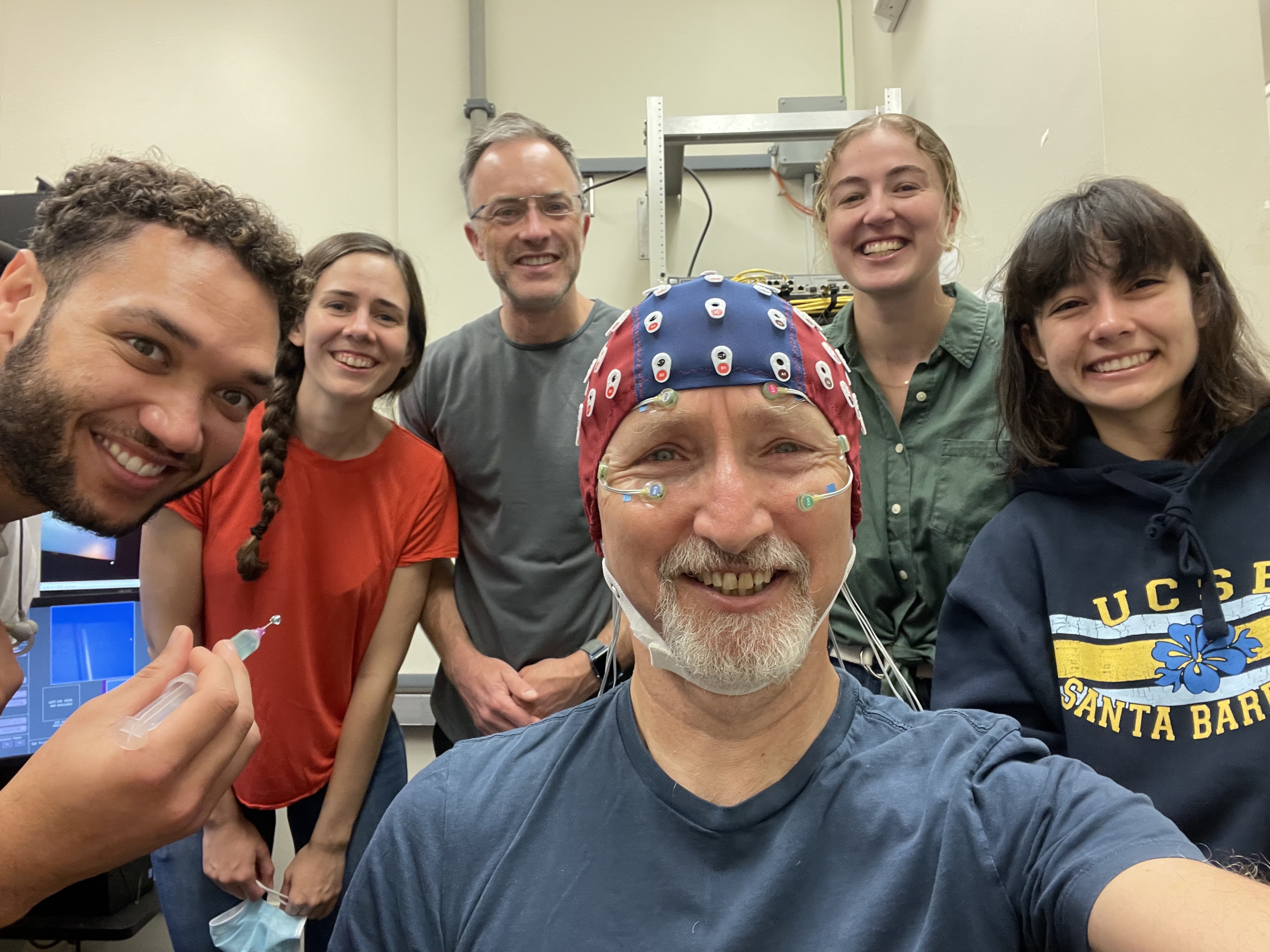 Barry taking a selfie in an eeg cap, with lab members behind him